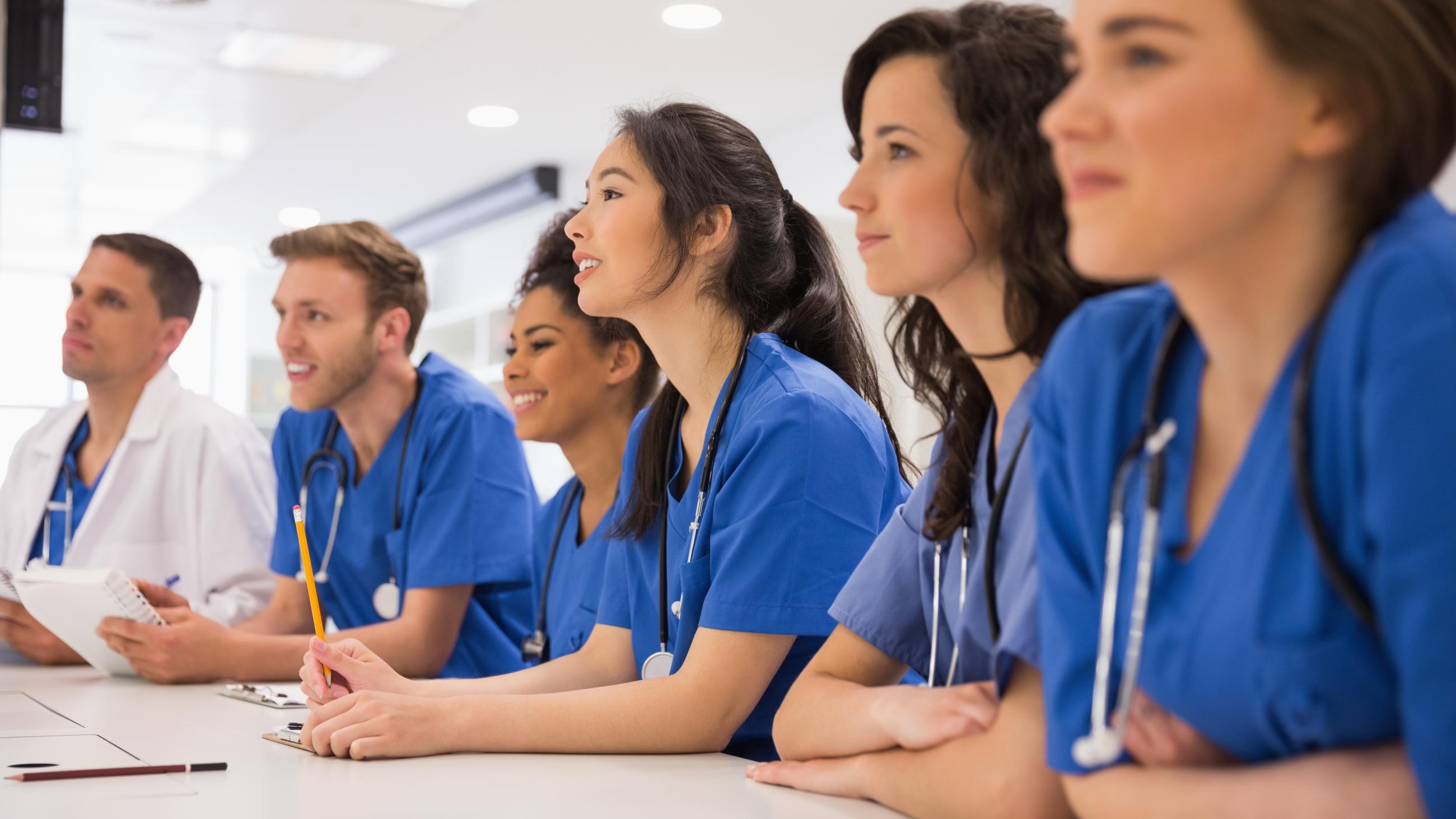 A group of people in scrubs sits at a table in a classroom