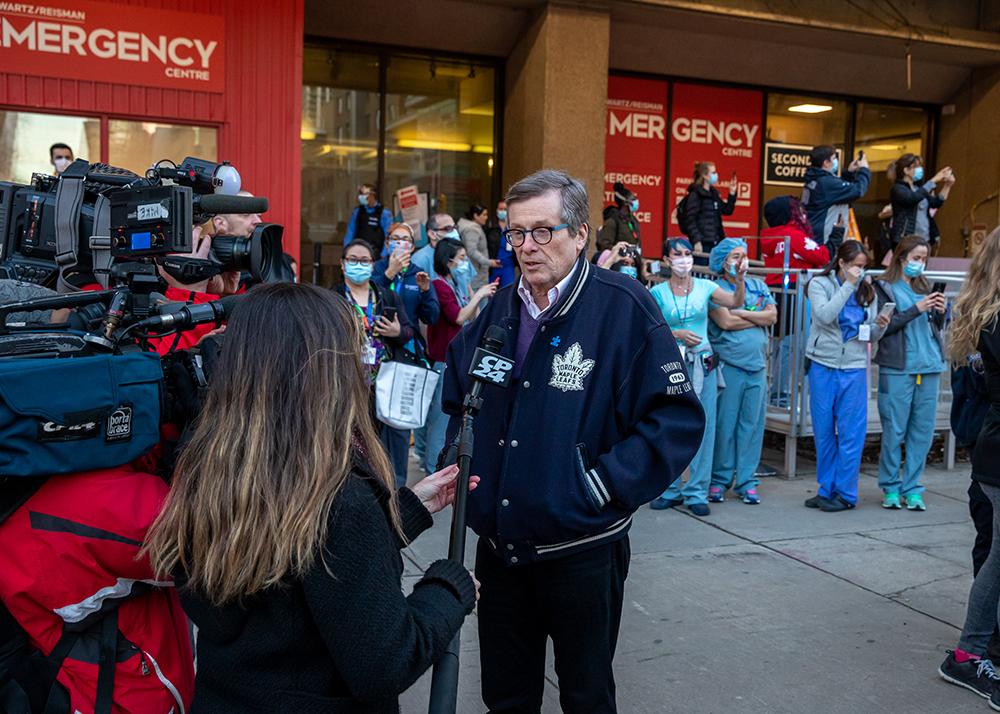 Toronto Mayor John Tory speaks with the media outside Mount Sinai Hospital's emergency department. Health-care workers stand in the background.