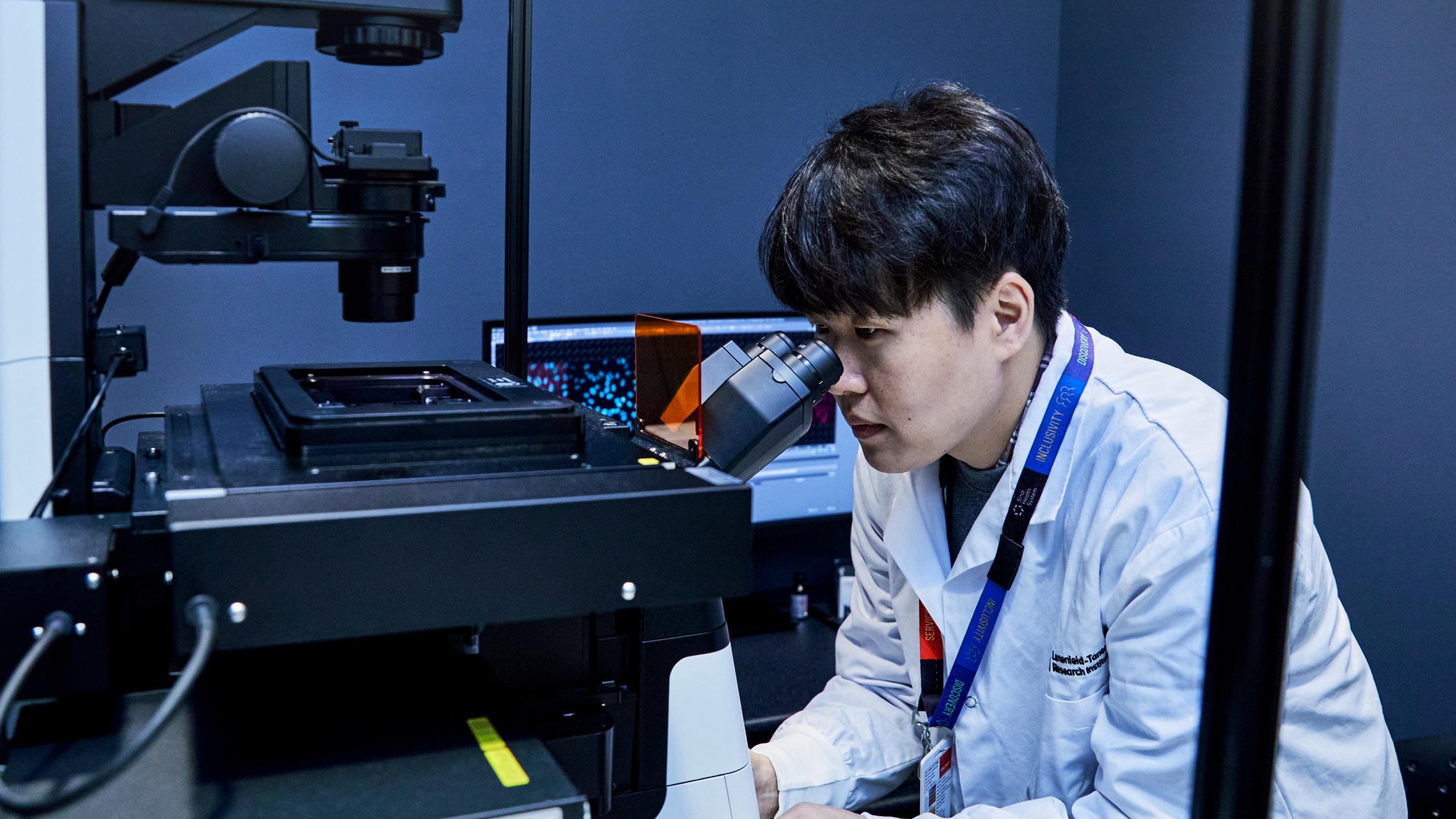 Man in a lab coat looking into a microscope in a laboratory