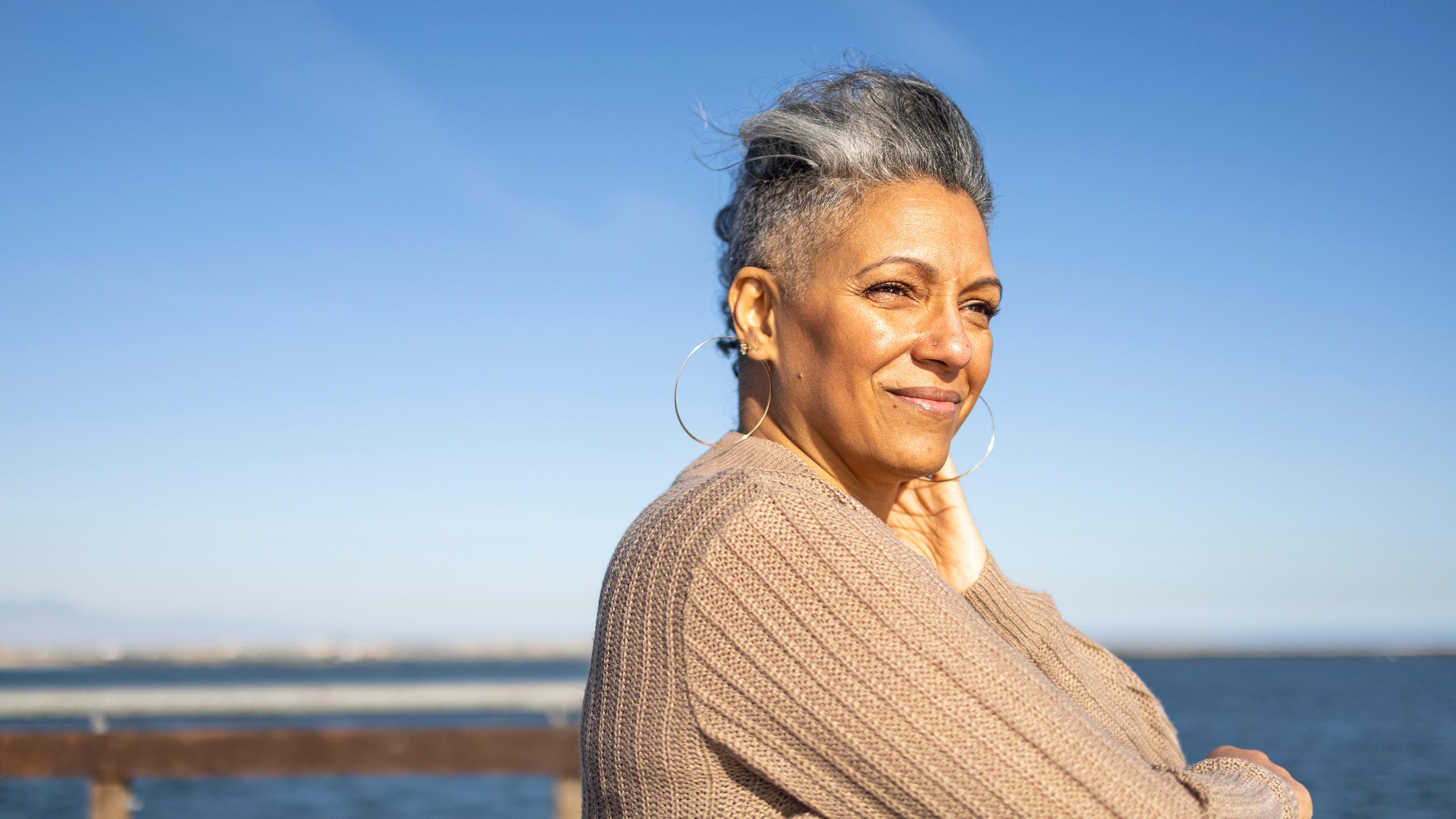 Older woman stands outside by a body of water