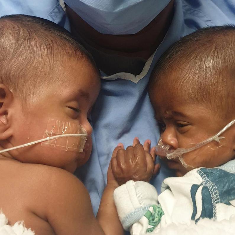 two babies lay face to face, holding hands