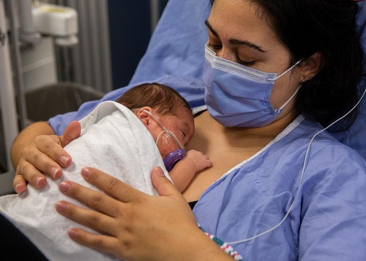 Woman wearing mask holds newborn on her chest