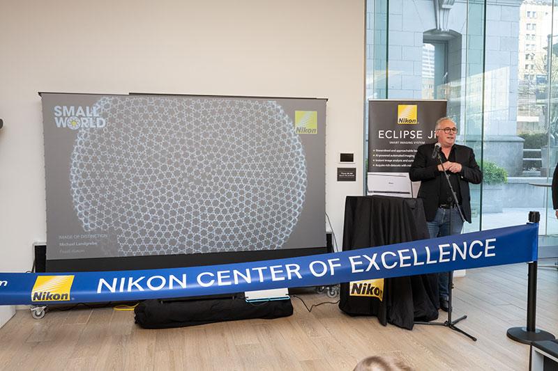 Man stands at podium behind blue banner that says 'Nikon Center of Excellence'