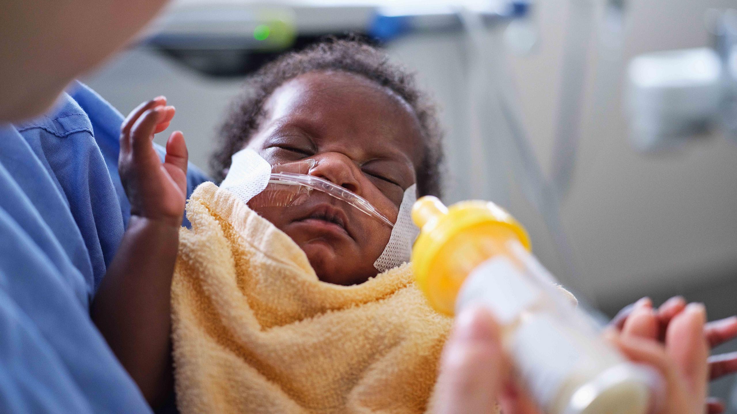 Infant being held by someone holding a bottle feeder