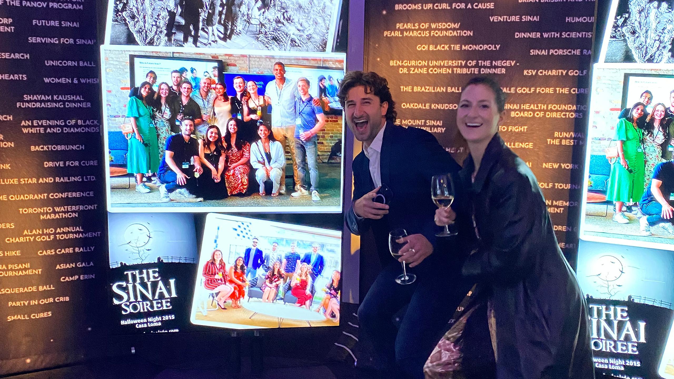 Two people posing and laughing in front of a screen with other photos