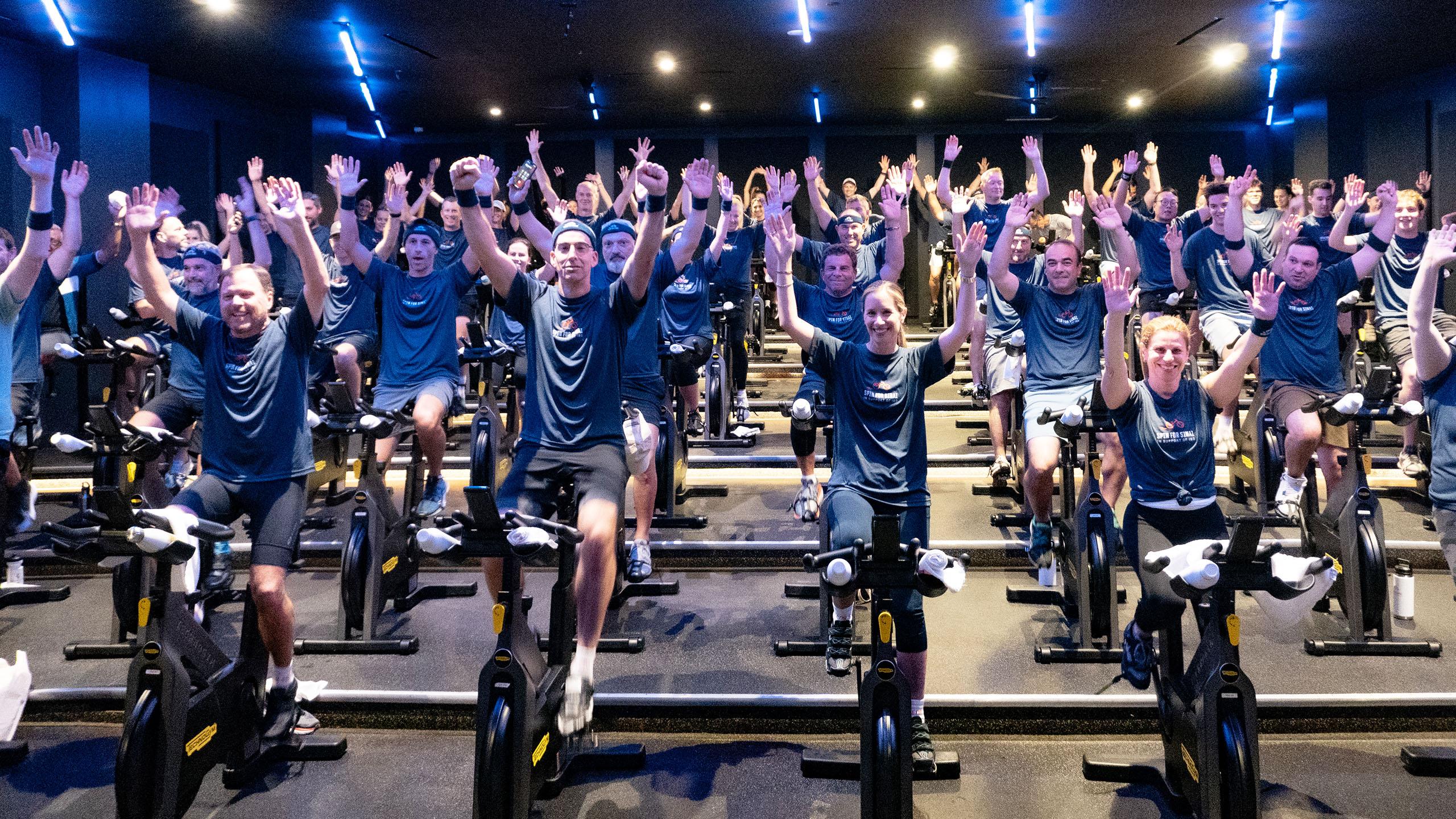 A group of people on spin bikes with their arms up in celebration