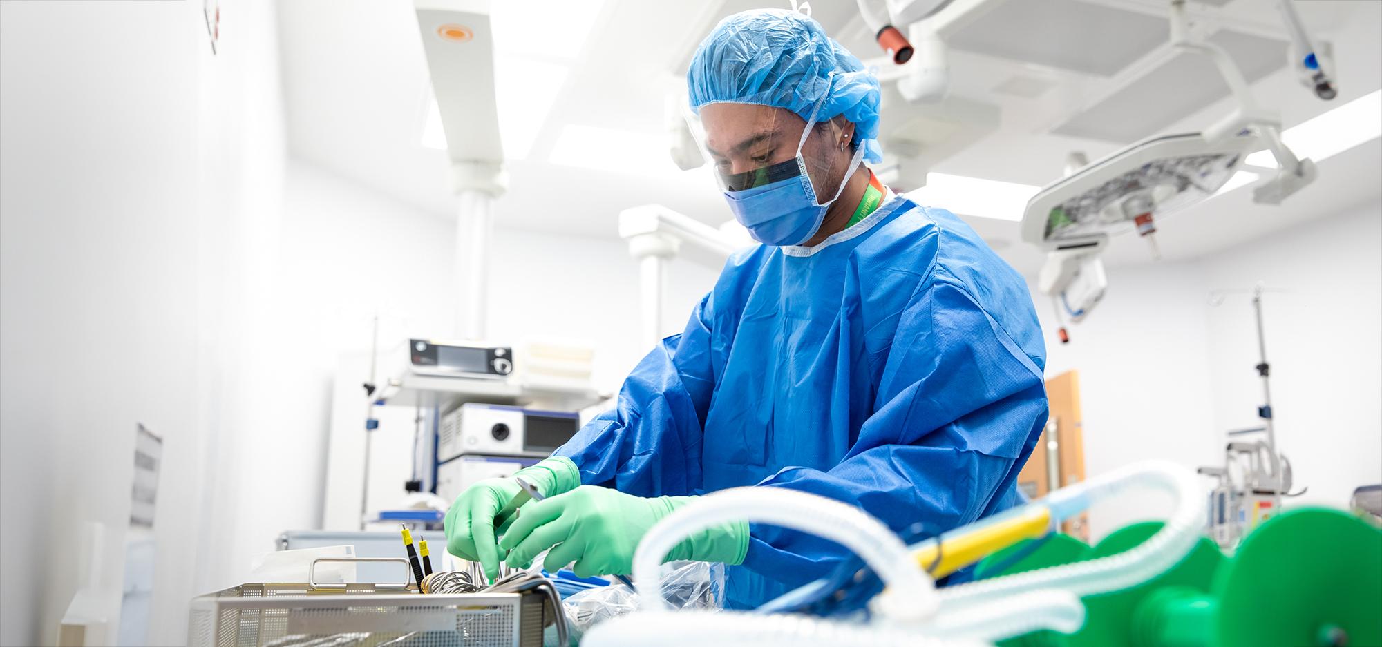 A hospital staff member is gowned up and going through surgical instruments in a surgical operating room.