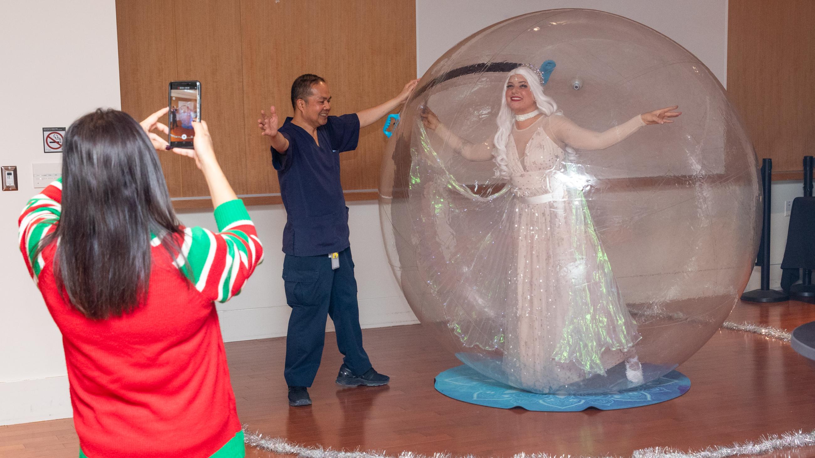 A staff member poses next to a performer inside an inflatable snow globe during Sinai Health’s Holiday Open House.