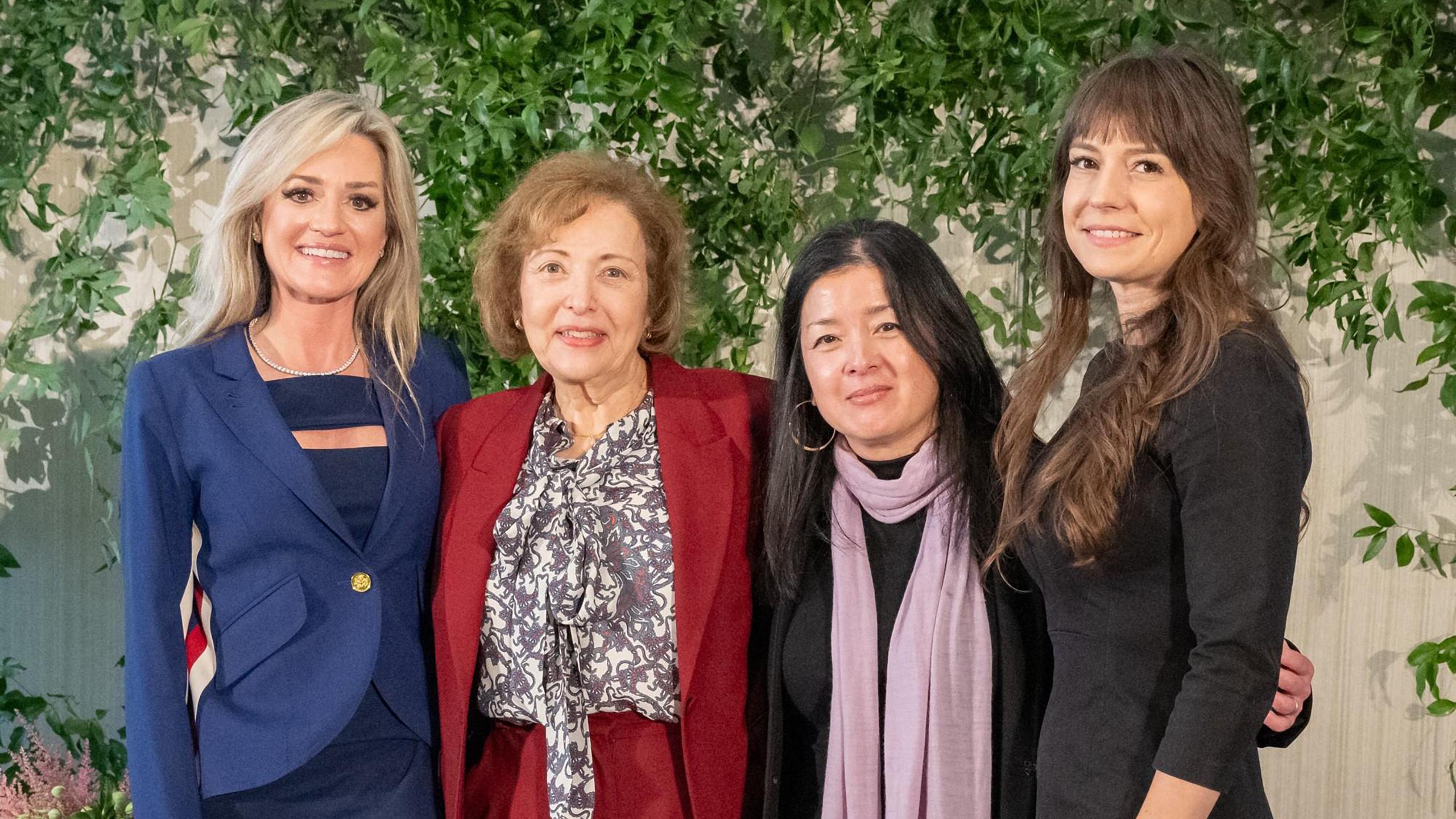 four women posing in front of a wall of plants