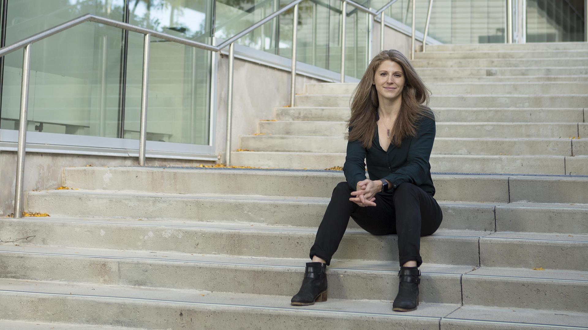 Woman sitting on the steps outside a glass-walled building