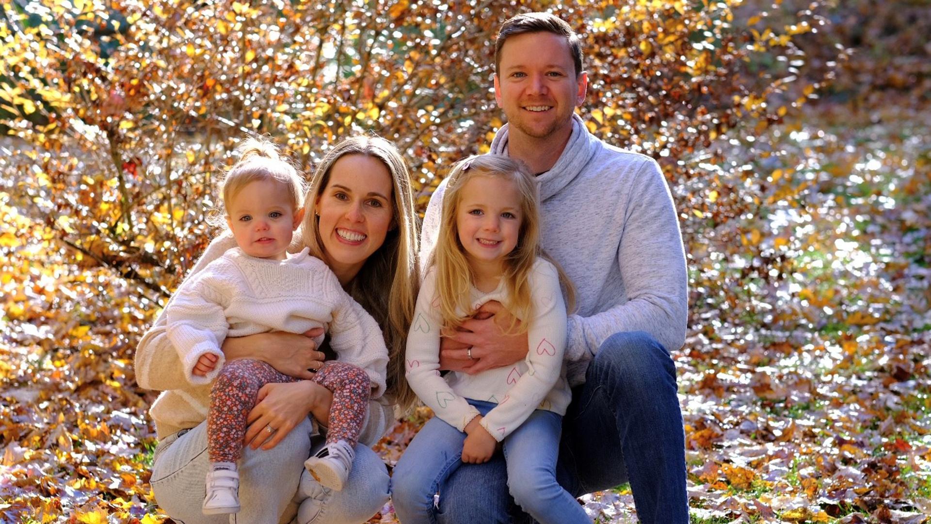 Jami Baker with her two children and husband with fall foliage in the background.