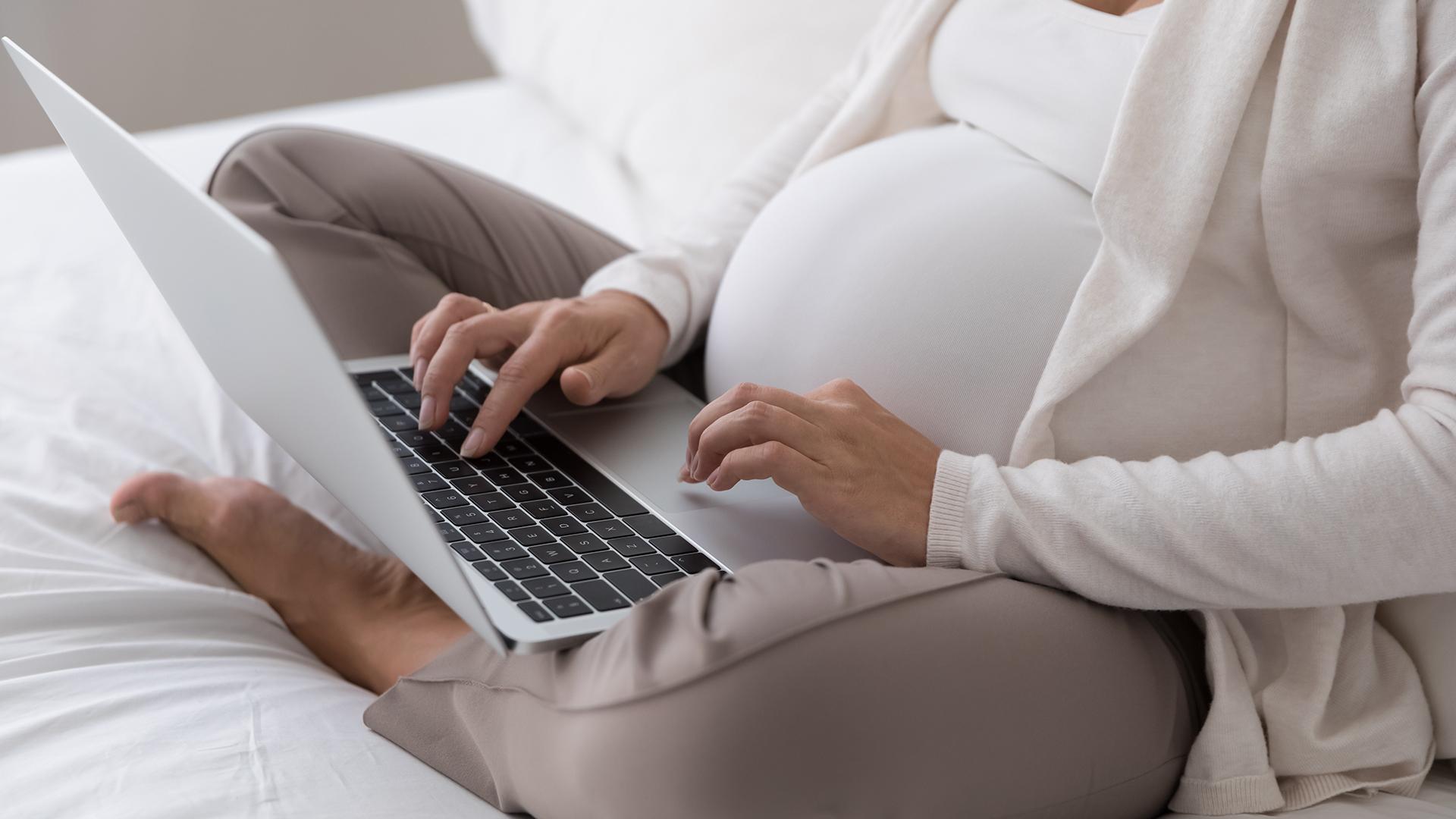 Pregnant woman using a laptop on her lap.