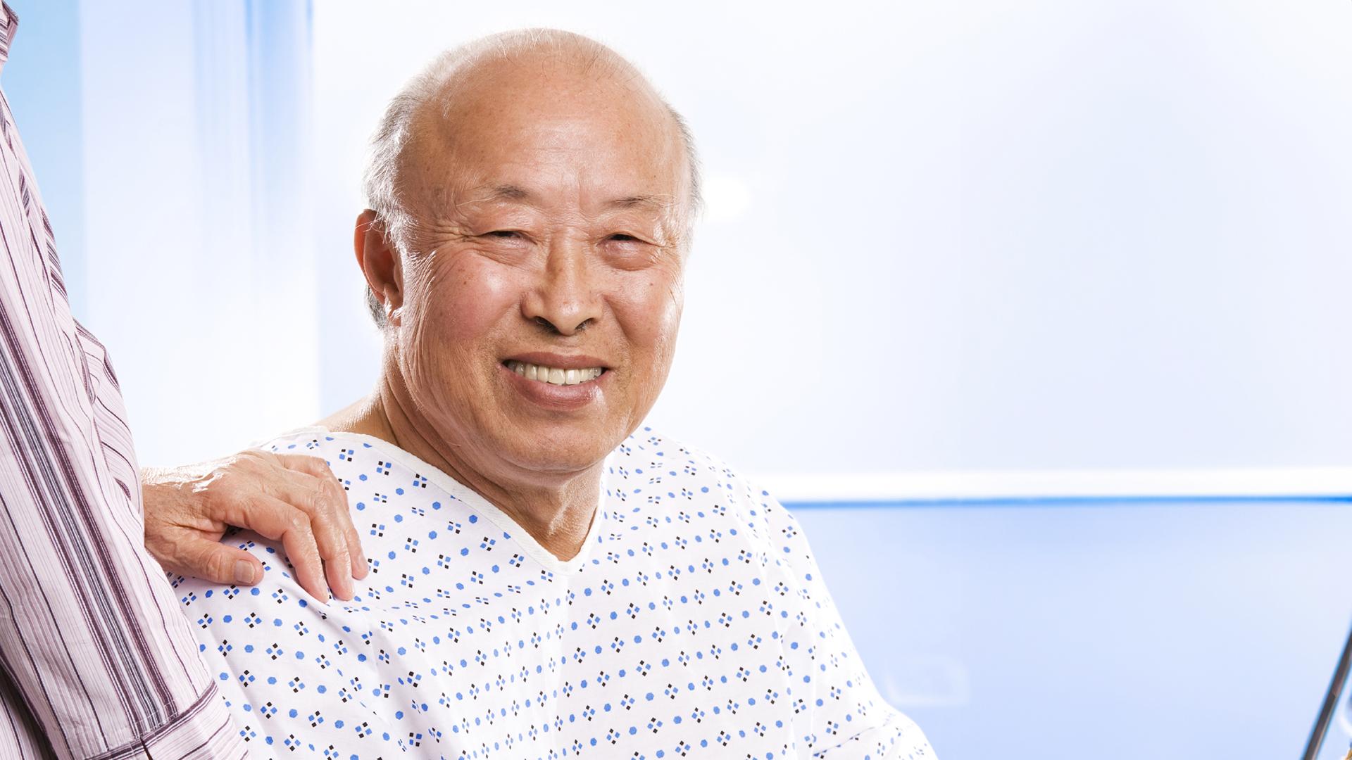 Senior Asian man with hand of caregiver on shoulder.