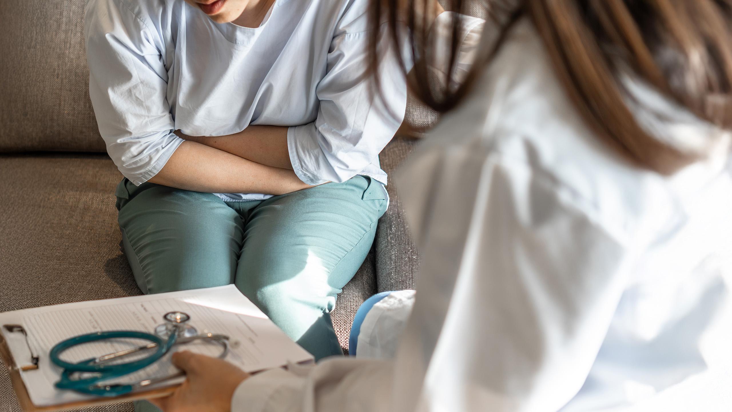 woman sits on couch holding abdomen