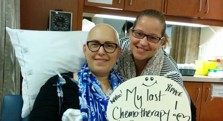 woman sits in hospital bed with sign that says, 'my last chemotherapy'