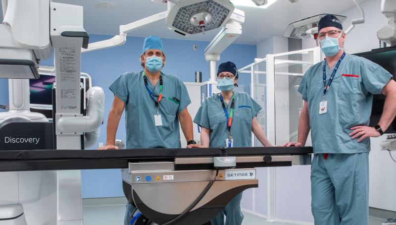 Three surgeons posing by an operating table