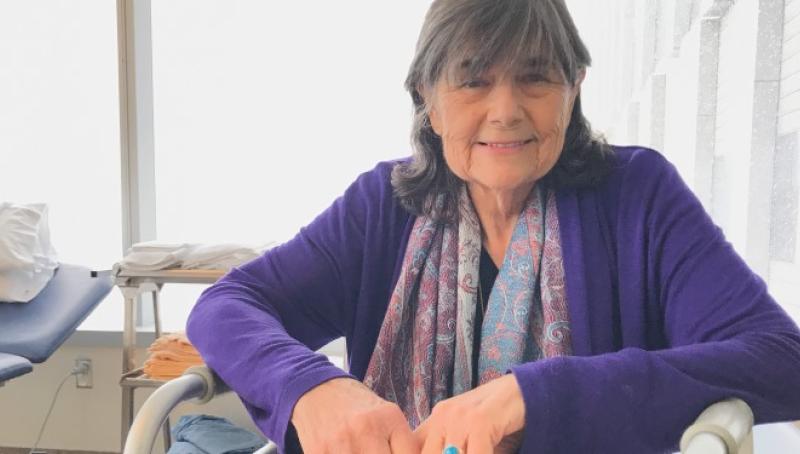 Mrs. Penn sitting in her hospital room smiling wearing a purple sweater.