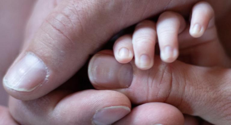 An adult's hand holding an infant's hand