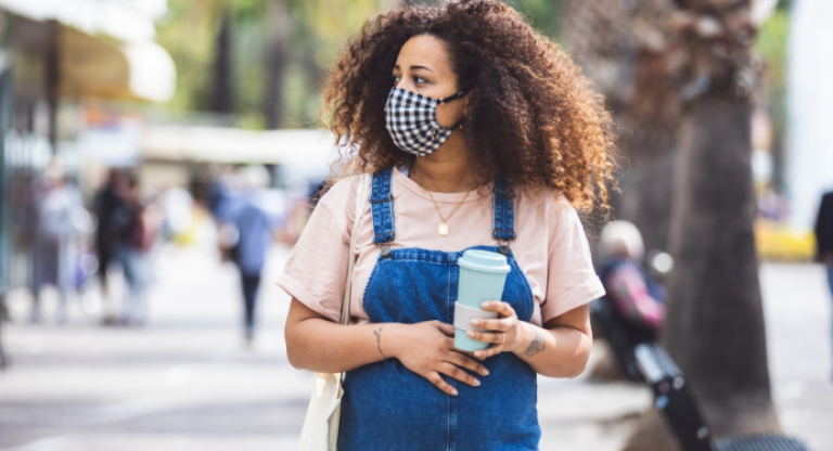 Pregnant woman is wearing a mask and holding coffee 