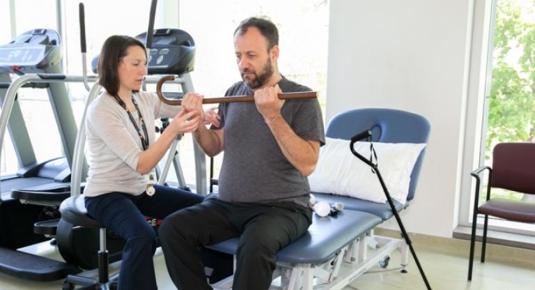 Physician helping man lift cane with both hands at rehabilitation centre. 