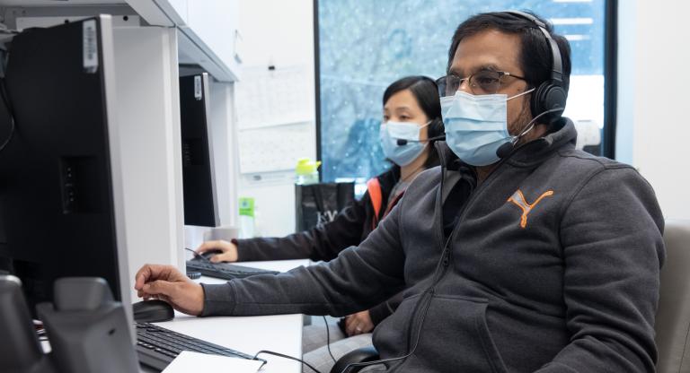 Two individuals wearing facemasks using computers