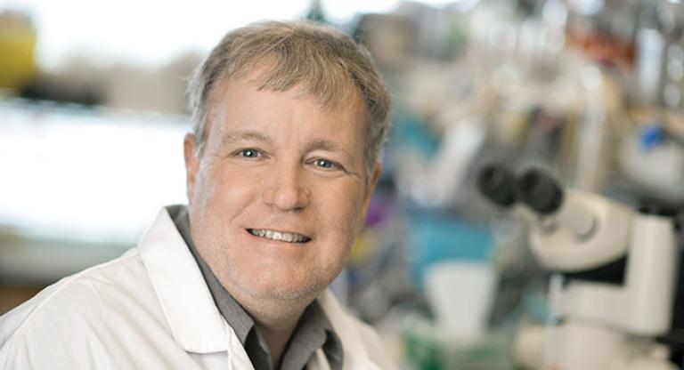 Man in lab coat in front of a microscope.