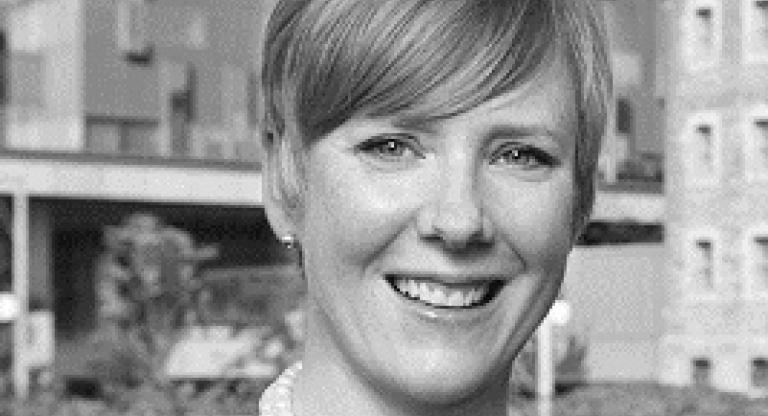 A headshot of a woman with a hospital in background