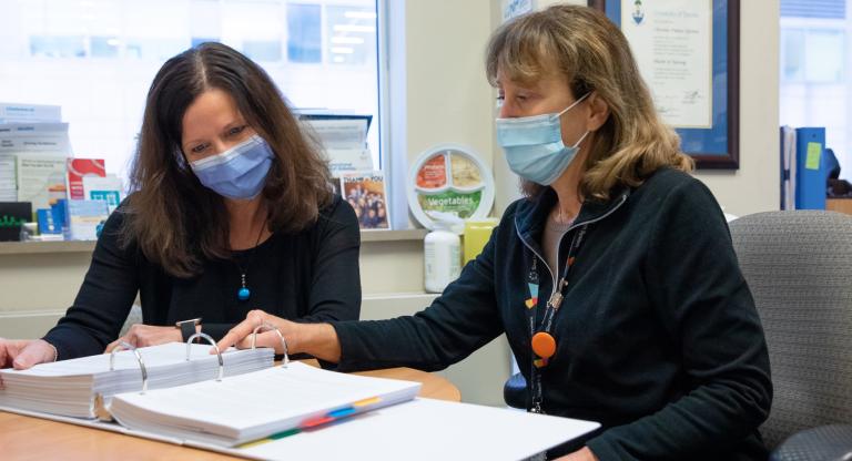 Two women wearing face masks sitting down together and reading