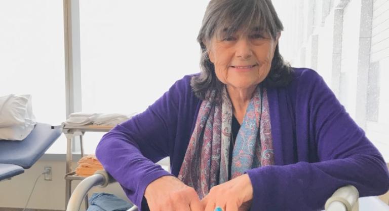 Mrs. Penn sitting in her hospital room smiling wearing a purple sweater.