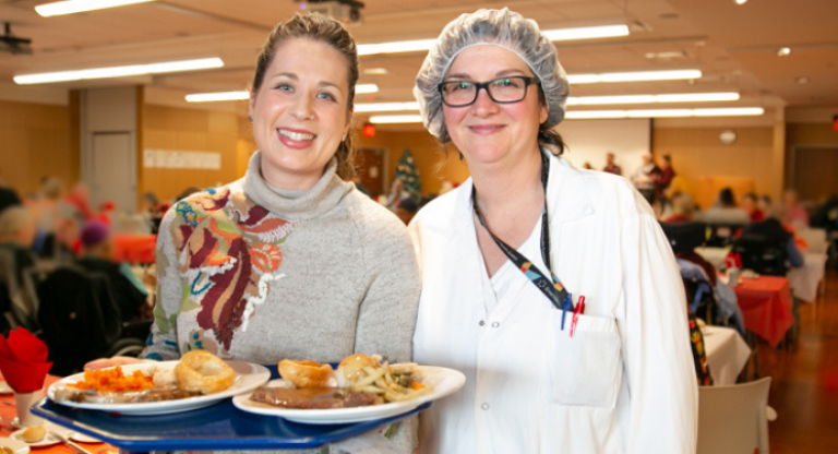 Two women with plates of food at the annual patient holiday meal event.