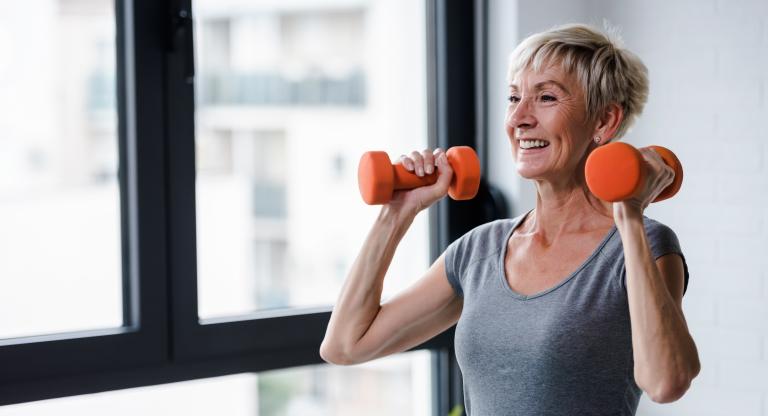 A woman lifts two orange dumbbells