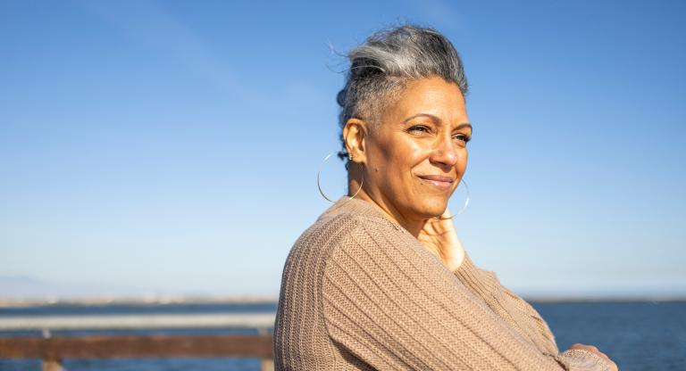 Older woman stands outside by a body of water