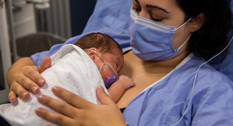 Woman wearing mask holds newborn on her chest