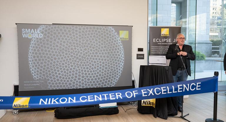 Man stands at podium behind blue banner that says 'Nikon Center of Excellence'