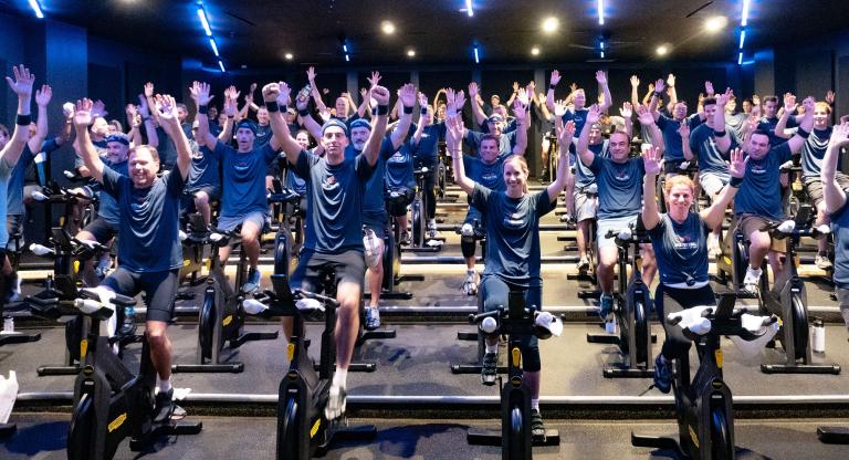 A group of people on spin bikes with their arms up in celebration