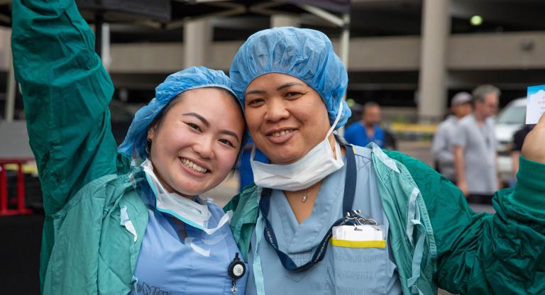 Two smiling people in scrubs outdoors