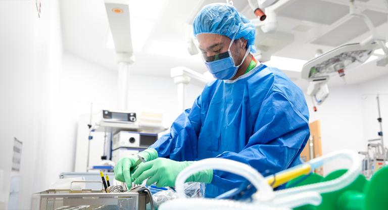 A hospital staff member is gowned up and going through surgical instruments in a surgical operating room.