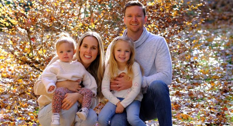 Jami Baker with her two children and husband with fall foliage in the background.