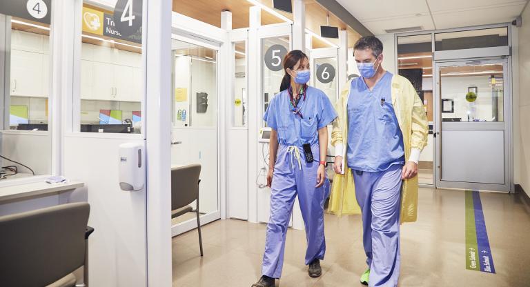 Two doctors in scrubs, walking side by side down the hallway of the Emergency Centre.