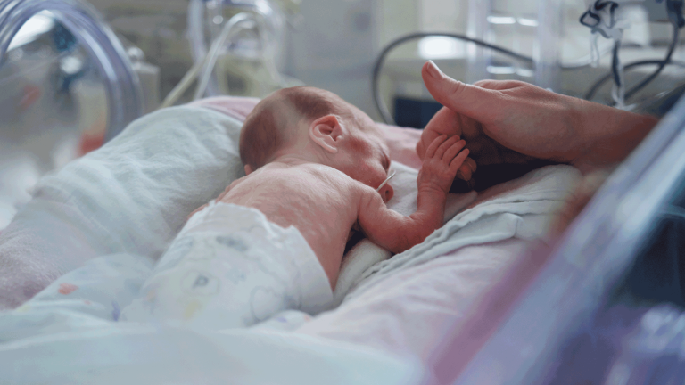 Small baby in incubator holding her mother's finger