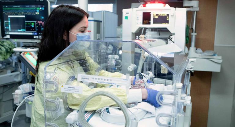 Female nurse with her arms in an incubator with a baby inside 