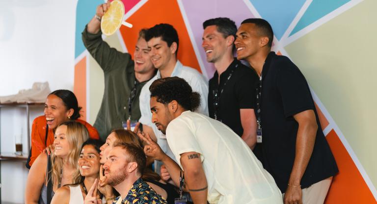 Group of people posing and smiling in from of a colourful backdrop