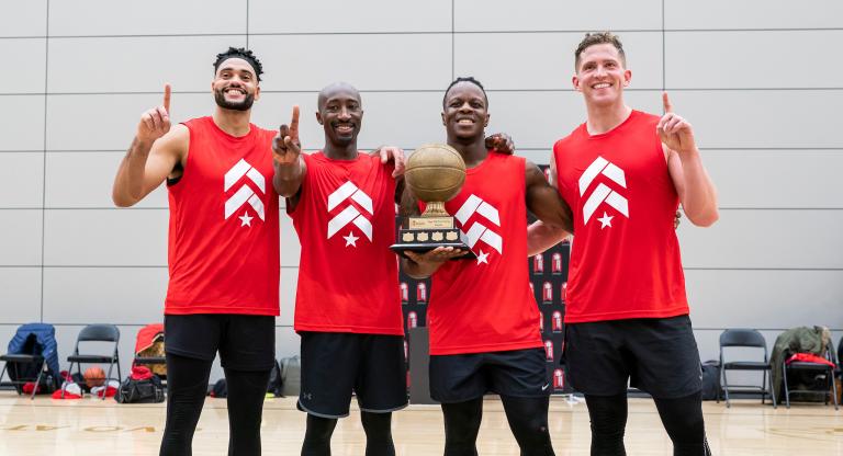 Four men in basketball jerseys posing with a trophy