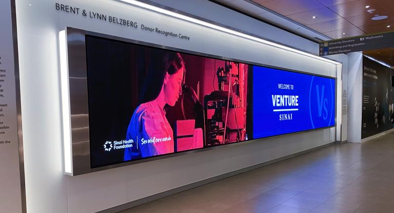 Large screen with photo of a researcher and a logo that says venture sinai