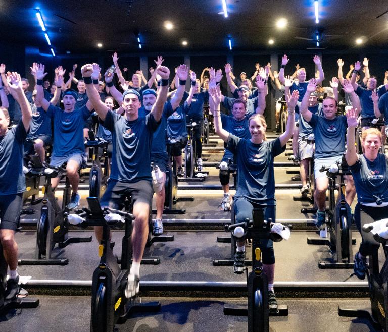 A group of people on spin bikes with their arms up in celebration